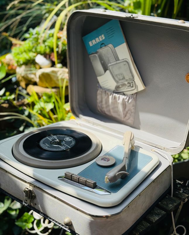 Erres koffergrammofoon met opengeklapt deksel en een single op de draaitafel, buiten tussen planten