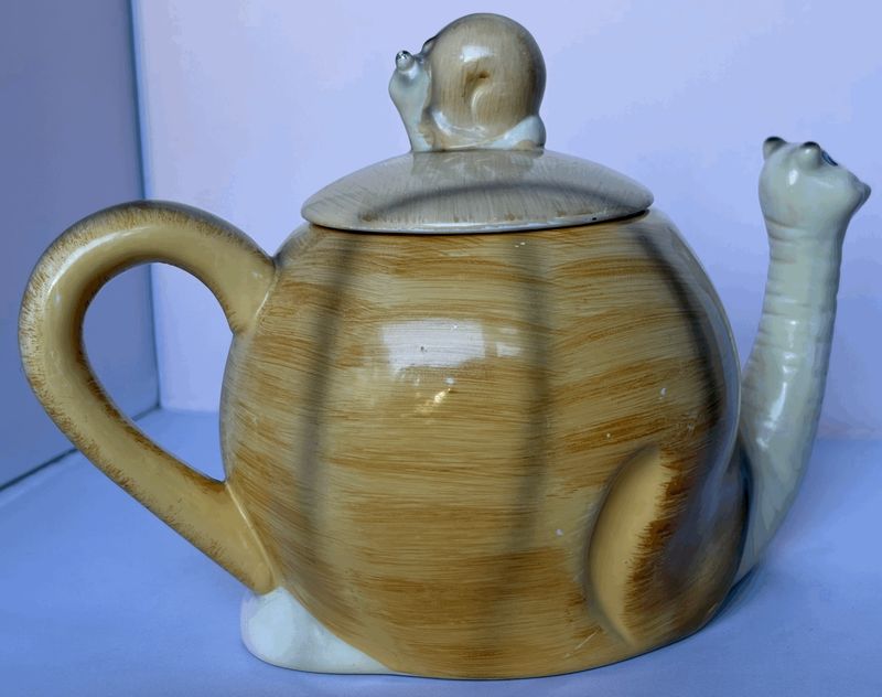 De theepot van opzij: okergeel met de slakkenkop als tuit en het oor als staart
