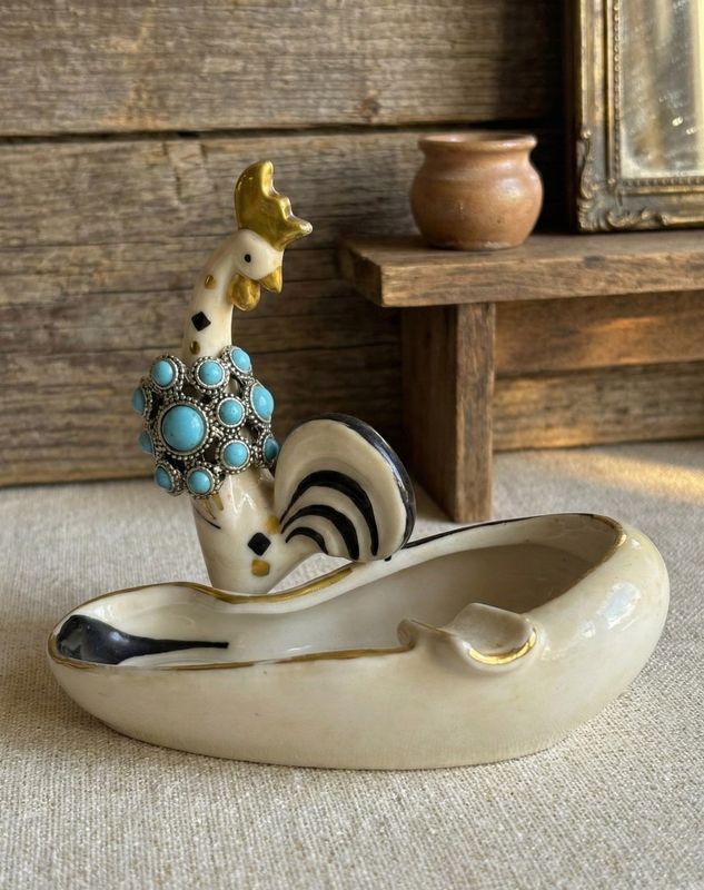 Ring met turkooisblauwe stenen om de hals van een keramisch haantje op een schaaltje