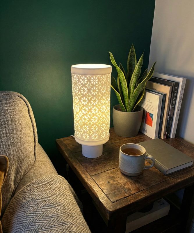 Brandende tafellamp met opengewerkte witte keramieken kap op een houten bijzettafel