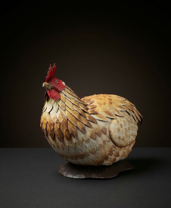 Zittende kip van metaal met geschilderde veren en een rode kam
