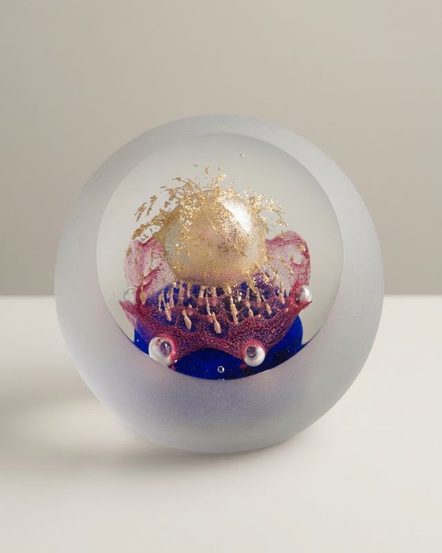 Mat glazen presse-papier met een gouden bol boven roze en blauw glas