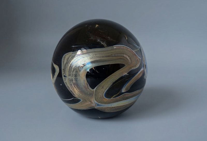 Detail van Mdina glazen presse papier met vloeiende swirl en lichte metallic gloed