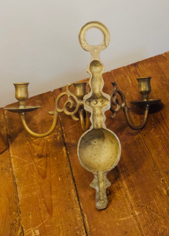 Vintage messing wandkandelaar met drie armen, bolvormige kern en sierlijke krulmotieven van de achterkant.

