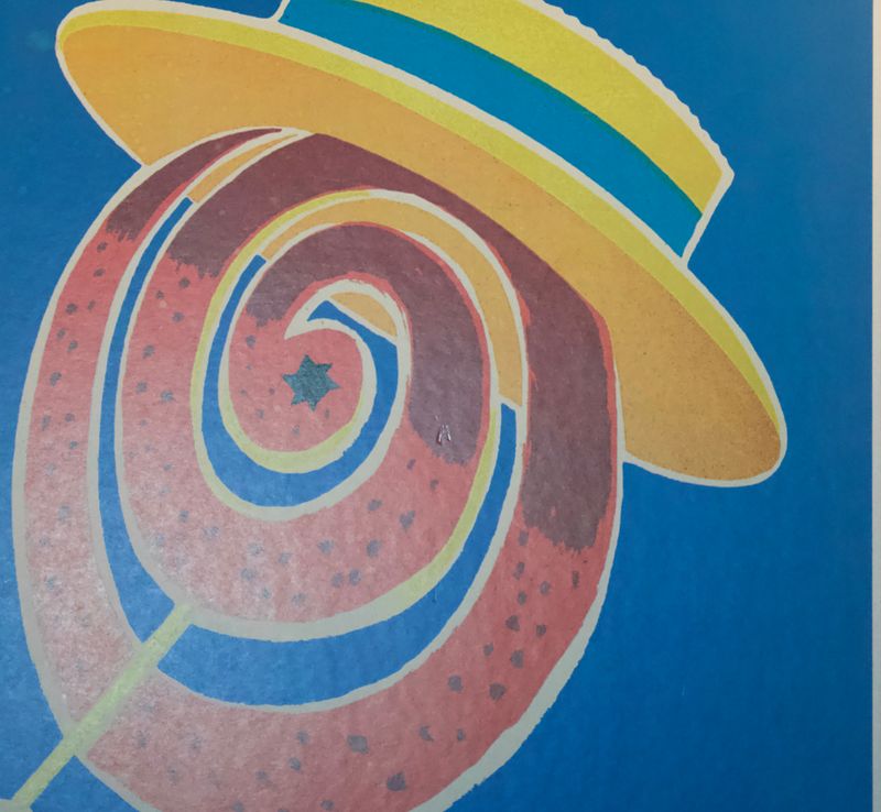 Close‑up van kleurrijke spiraal en hoed op vintage Orangina reclameposter met rood‑gele details en een kleine beschadiging.