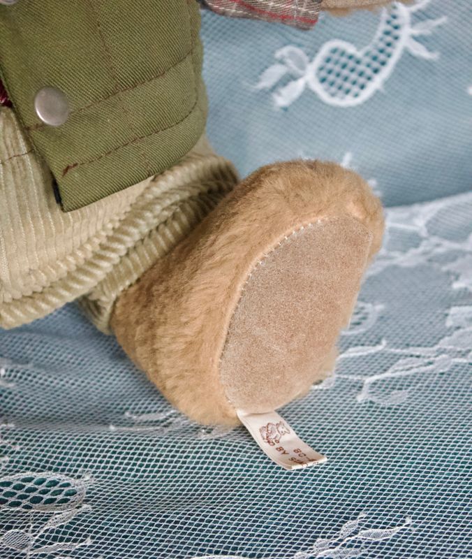 Close‑up van het label aan de voet van de teddybeer, corduroy broek.
