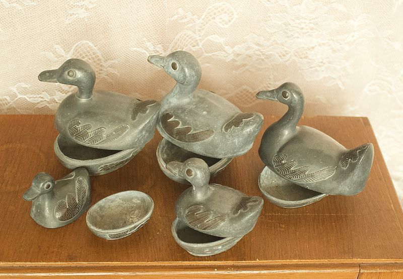 Geopende tinnen eenden opbergdoosjes met afneembare deksels op houten ondergrond.