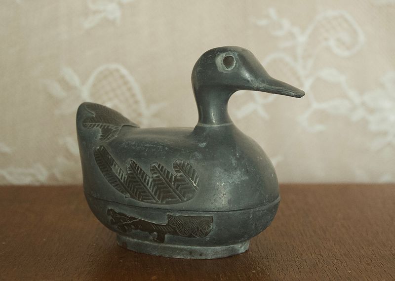 Zijaanzicht van grote tinnen eend doos met reliëfdetails van vleugels op de basis.
