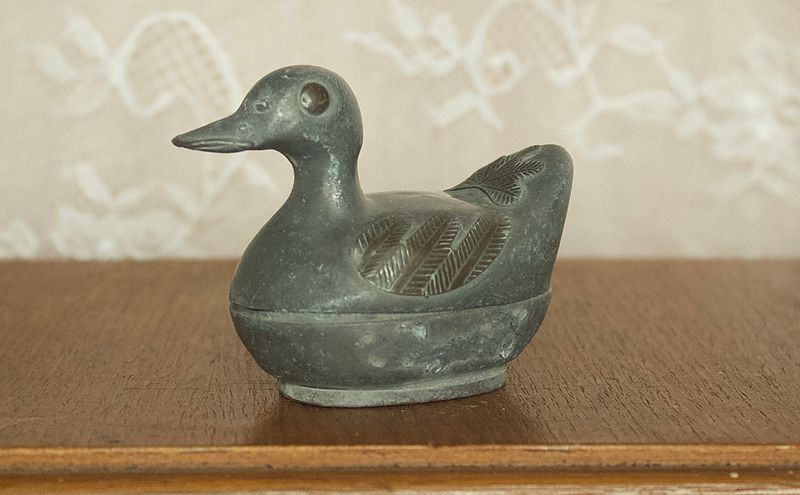 Zijaanzicht van grote tinnen eend doos met reliëfdetails van vleugels op de basis.