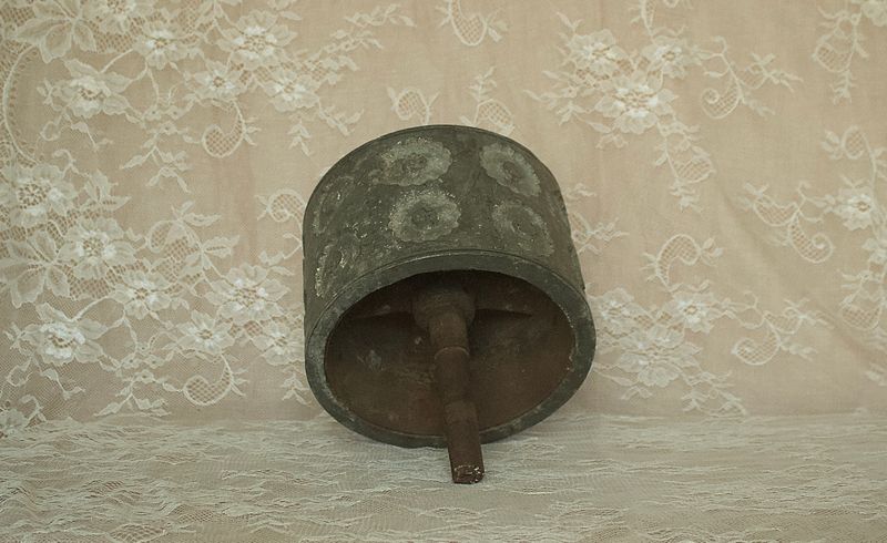 Zijaanzicht van een antieke metalen deegroller met verhoogde rozetpatronen en een lange metalen as