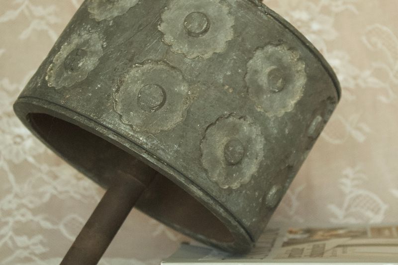 Detailopname van een antieke metalen deegroller, die de patina en verhoogde rozetpatronen op het oppervlak laat zien