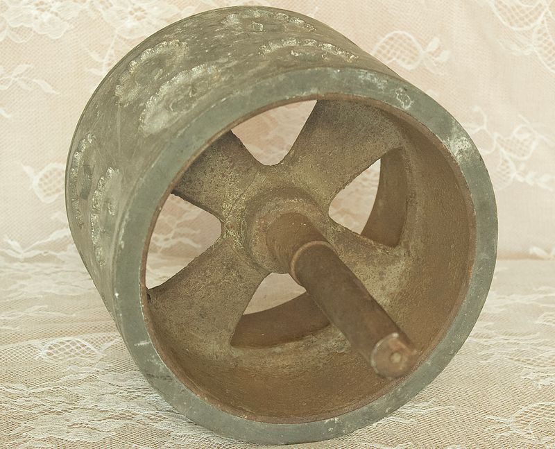 Antieke metalen deegroller, die de binnenstructuur, de centrale as en de spaken laat zien.