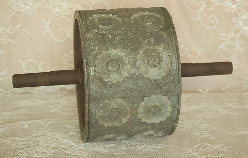 Detailopname van een antieke metalen deegroller, die de patina en verhoogde rozetpatronen op het oppervlak laat zien