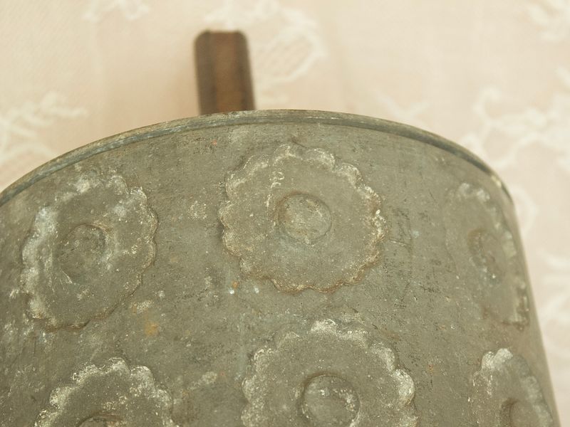 Detailopname van een antieke metalen deegroller, die de patina en verhoogde rozetpatronen op het oppervlak laat zien