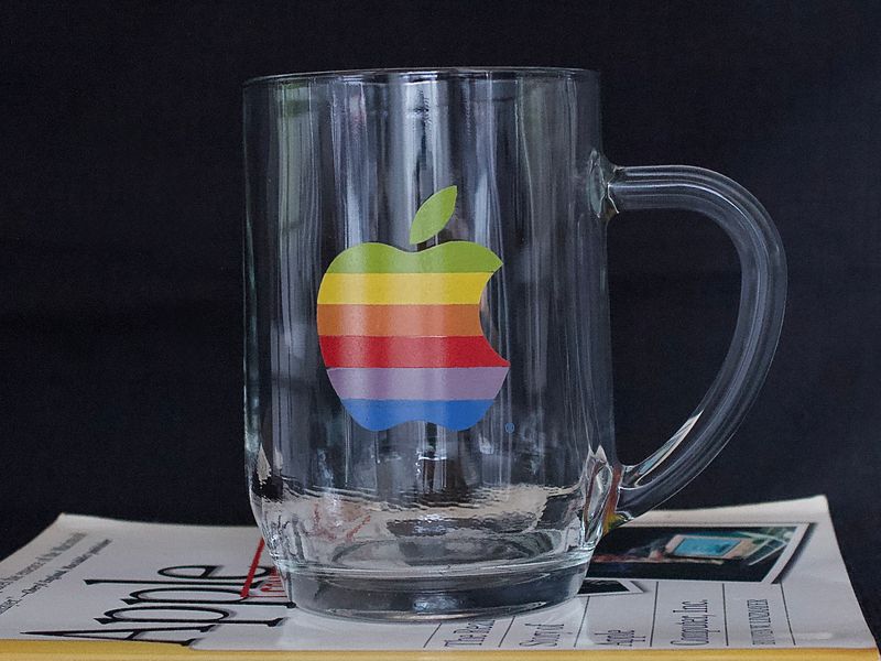 Glazen mok met het Apple-logo in regenboogkleuren, op een krant