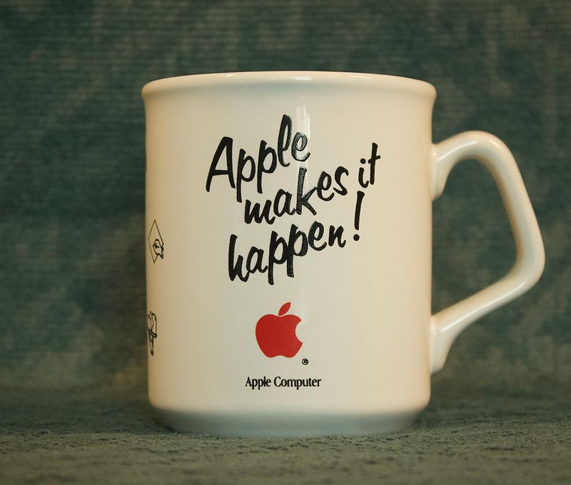 Witte mok met de tekst Apple makes it happen en het rode Apple-logo