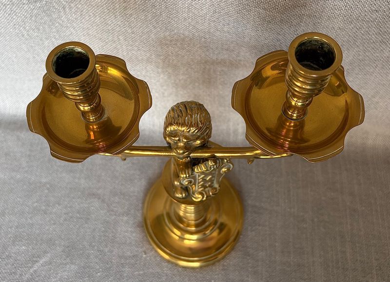 Schuin bovenaanzicht van de messing kandelaar met zicht op de twee kaarsenhouders, lekschalen en leeuwenkop.