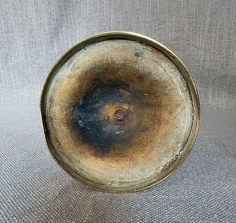 Onderkant van de ronde messing voet met de centrale bevestigingsmoer, sporen van oxidatie en patina.