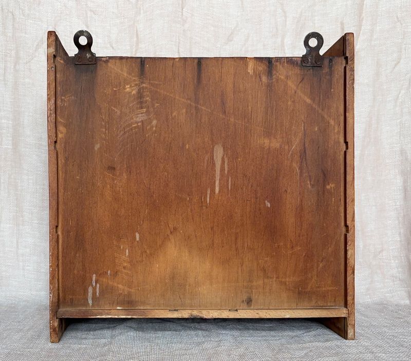 Achterzijde van het houten kastje met vlakke houten achterwand en twee metalen ophangogen.