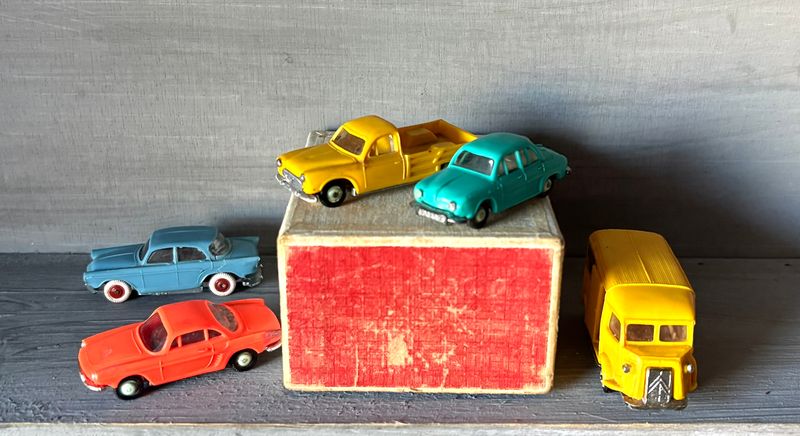 De vijf Norev-autootjes rond het originele doosje: twee gele, een groene, een blauwe en een rode