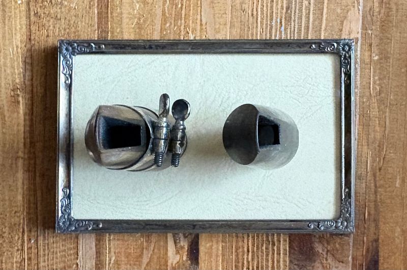 Mondstuk en beschermdop in een zilverkleurig lijstje aan een houten wand