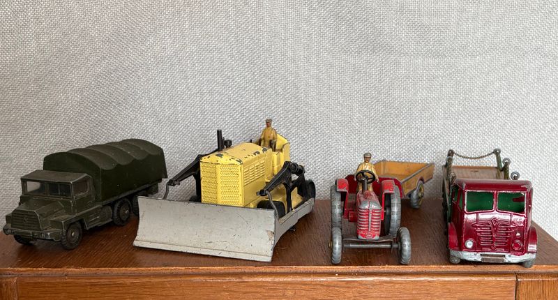 Vier Dinky-modellen op een rij: legertruck, gele bulldozer, rode tractor en kraanwagen